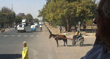 Straße mit regem Verkehr in Addis Abeba. Zu sehen sind Autos, Menschen und ein Kutsche.