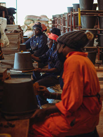 Frauen arbeiten an der Herstellung von Tonfiltern in Uganda und lächeln dabei.