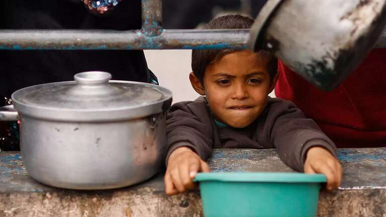 Ein kleines Kind hält eine Schüssel mit ausgestreckten Armen und wartet auf die Verteilung von Essen