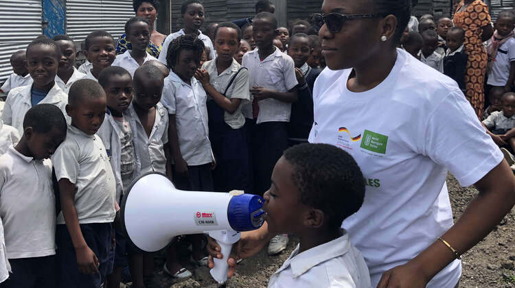 Schulung zur Prävention von Ebola an einer Schule nahe Goma, D. R. Kongo. Ein Kind spricht bei einer Schulung über Ebola in ein Megafon.
