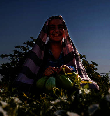 Frau sitzt in einem Feld und hält Obst in der Hand.