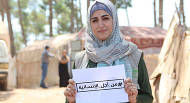 Frau in Syrien hält ein Schild mit einem Hashtag auf Arabisch