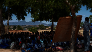 2019-gesundheitsclubs-kinder-training-malawi-lycka-welthungerhilfe-2.png Ein Mann hält einen Vortrag, Kinder hören zu.