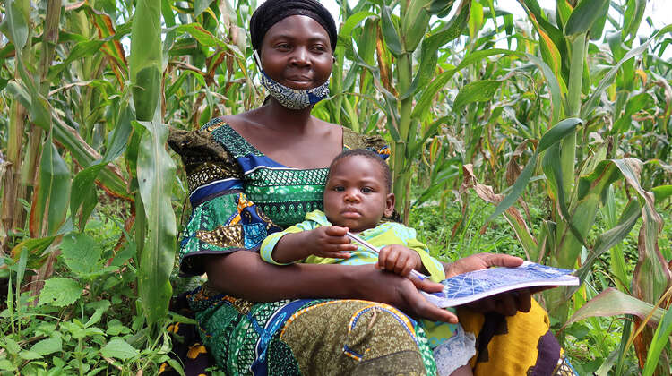 2021-dr-congo-projektteilnehmerin-furaha-mauwa-yoboka-auf-maisfeld.jpg Eine Frau sitzt mit ihrem Kleinkind am Rande eines Maisfeldes, Kongo 2021.