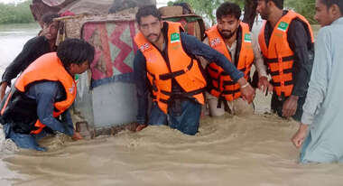 Überschwemmungen in Pakistan. Männer mit Schwimmwesten tragen einen großen Container durch kniehohes Wasser
