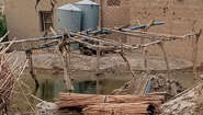Überschwemmungen in Pakistan. Ein Haus aus Lehm mit Rissen in den Mauern, im Vordergrund ist Wasser und Schlamm zu sehen.