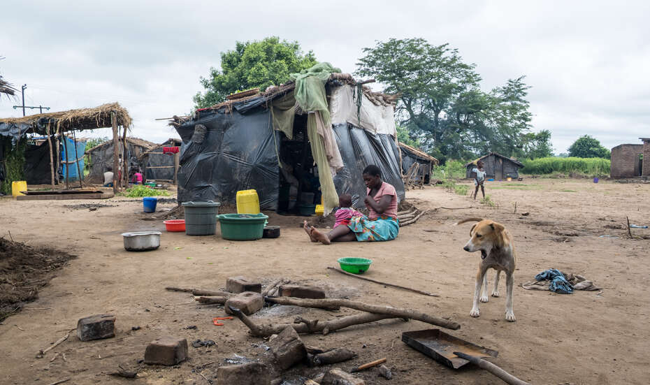 Nach Zyklon Idai in Malawi Eine Frau sitzt mit ihrem Kind auf dem Boden vor einer Hütte, die aus Planen und Decken gebaut wurde.