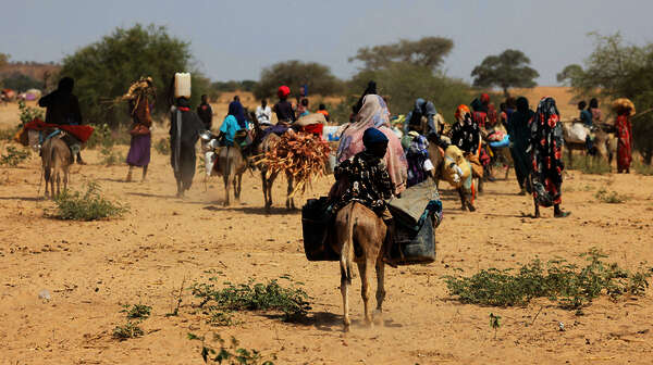 Sudanesische Flüchtlinge, die vor der Gewalt in der Region Darfur geflohen sind, suchen in Goungour, Tschad, vorübergehende Zuflucht. Das Bild zeigt Menschen, die zu Fuß und mit Eseln unterwegs sind und Gepäck tragen.