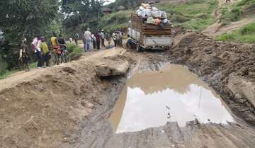 Straßenprobleme im Kongo Eine Straße mit einem riesigen Schlagloch voller Wasser. Ein Transporter hat Schwierigkeiten, fort zu kommen.