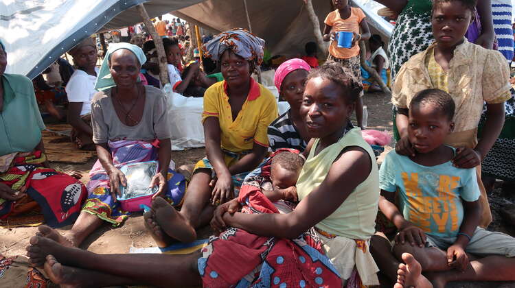 2019-4-wochen-nach-zyklon-idai-Zuflucht-unter-Planen-Aufnahmezentrum-Lamego-Mozambique-Bandsom-Welthungerhilfe.JPG Drei Frauen und fünf Kinder sitzen vor einer Plane, die als Notunterkunft aufgespannt wurde.