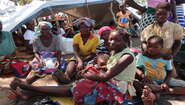 2019-4-wochen-nach-zyklon-idai-Zuflucht-unter-Planen-Aufnahmezentrum-Lamego-Mozambique-Bandsom-Welthungerhilfe.JPG Drei Frauen und fünf Kinder sitzen vor einer Plane, die als Notunterkunft aufgespannt wurde.