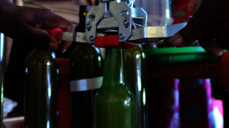 2019-sirup-kronkoren-aufsetzen-green-colleges-uganda-welthungerhilfe.jpg Jemand setzt einen Konkorken auf eine grüne Glasflasche.
