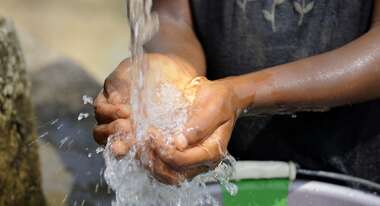 Zugang zu Wasser: Hände schöpfen Wasser unter einem Wasserstrahl.