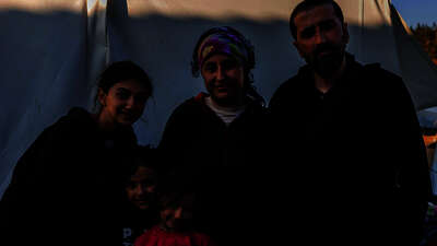 Erdbeben in der Türkei: Eine Familie steht vor einem Zelt, sie alle schauen in die Kamera.